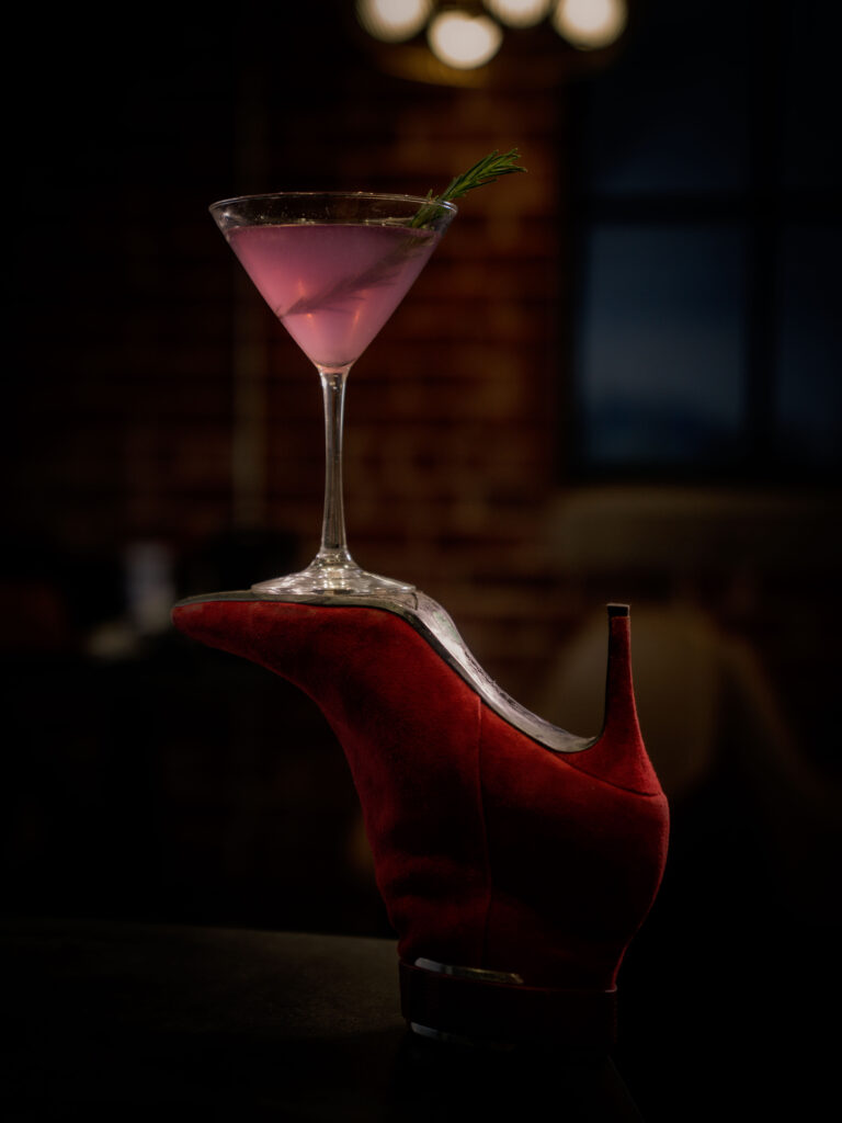 Pink cocktail displayed on a red high-heeled shoe during a creative branding shoot.