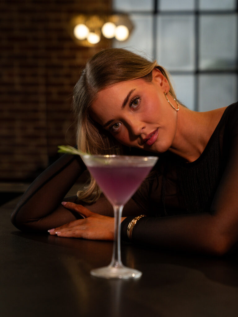 Woman posing beside a pink cocktail during a styled restaurant branding shoot.