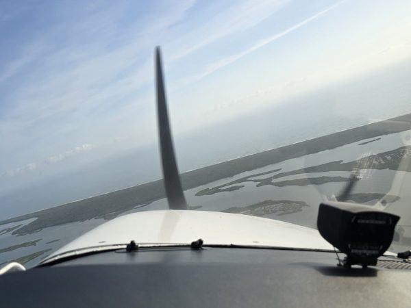 Propeller and wing of a small aircraft visible during flight above the landscape.