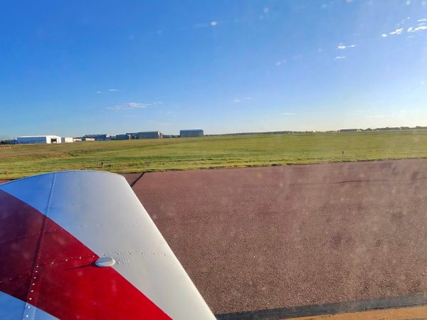 Red-and-white aircraft wing viewed from inside a small plane beside a runway.