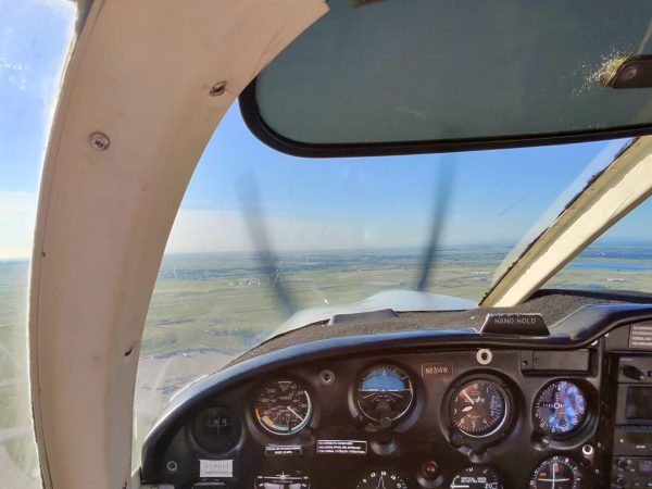 View inside a small aircraft cockpit with analog instruments, flight controls and the runway visible ahead.