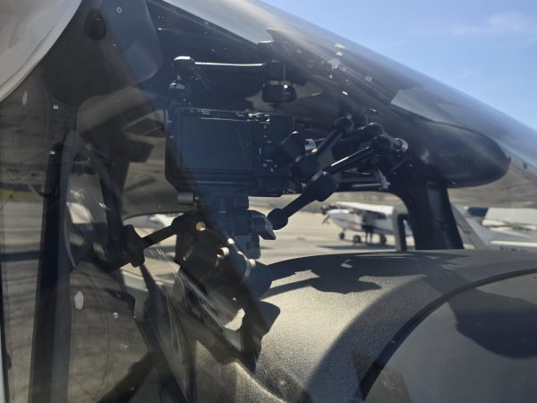 Camera rig positioned inside an aircraft with the wing and landscape visible during flight.